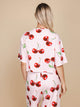 Vrouw met SNURK Mon Cherry Cropped T-Shirt Dames met kersenprint op een neutrale achtergrond.