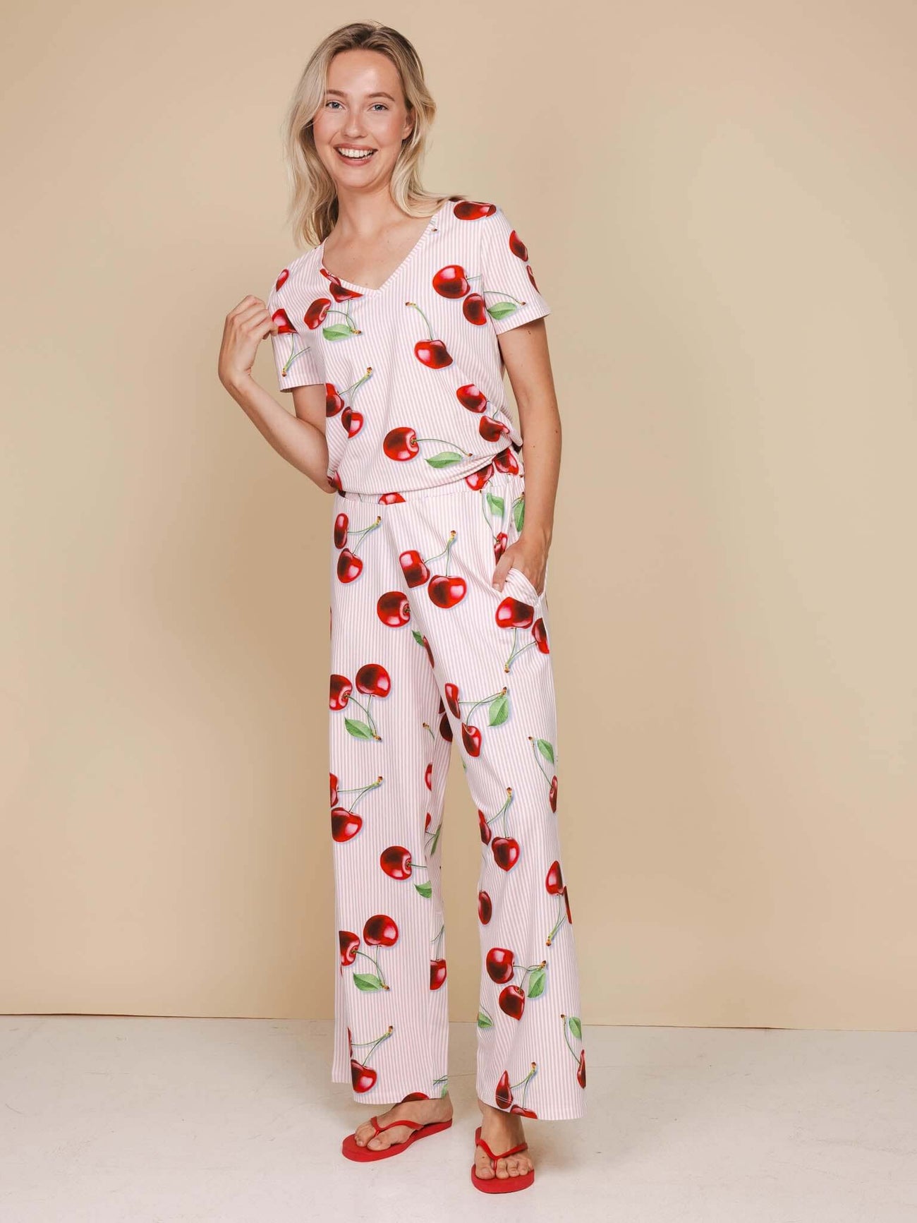 SNURK Mon Cherry Wijde Broek Dames in zachte katoen met kersenprint en wijde pijpen, model met vrolijke glimlach.