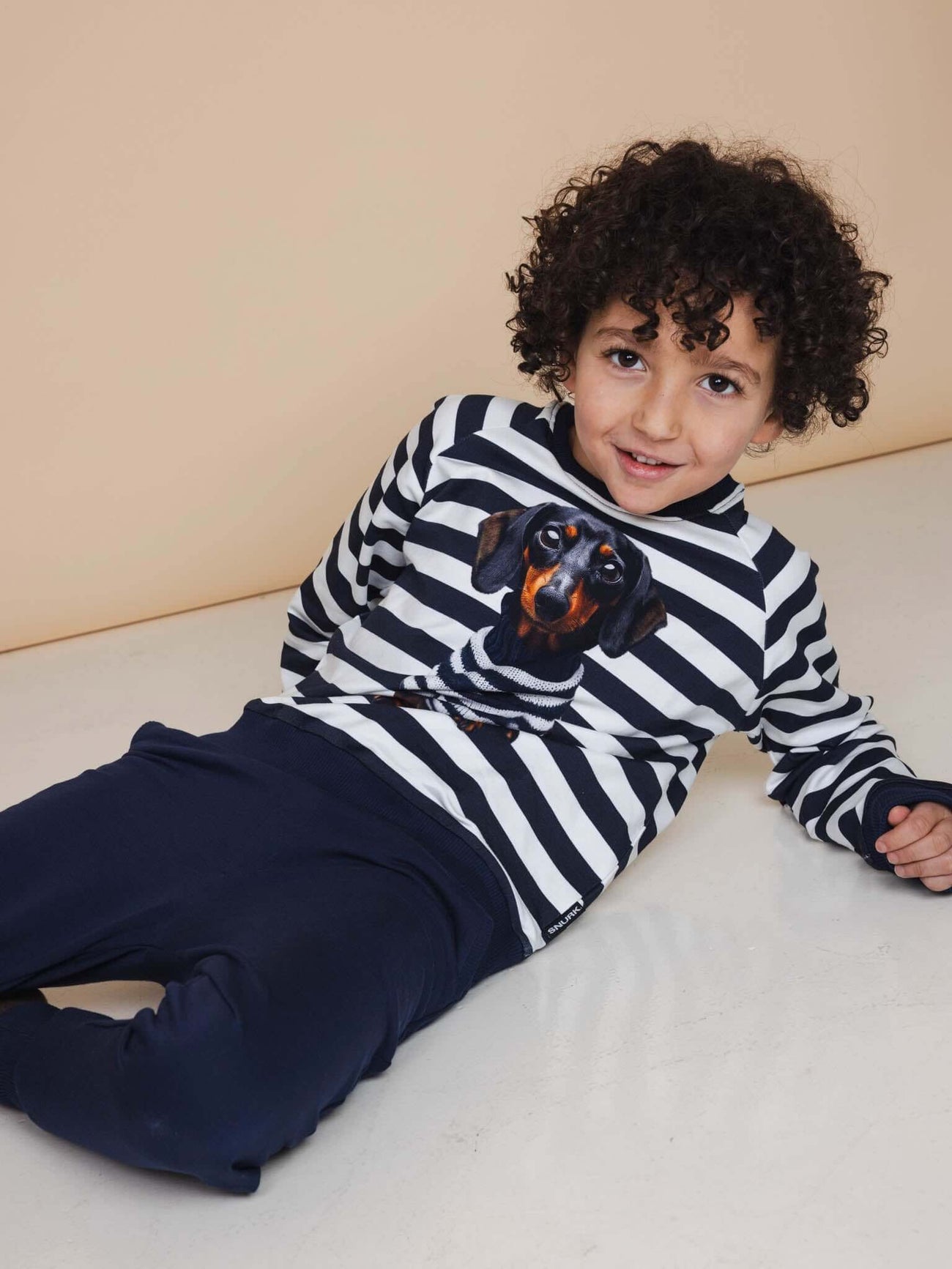 Kind met een hond op een gestreepte trui en SNURK Navy Broek Kids, relaxend op de vloer.