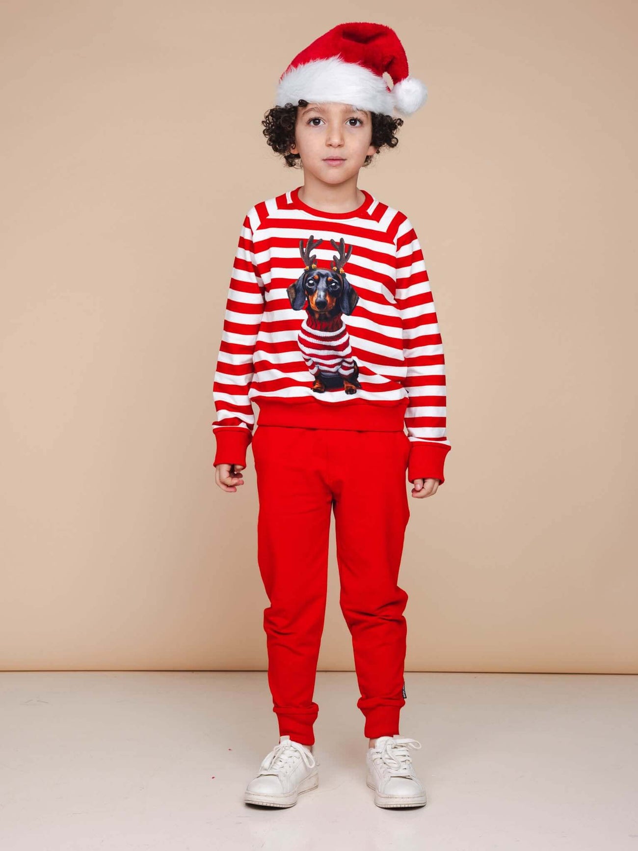 Kind in SNURK Pierre Xmas Sweater Kids met hond op de voorkant, kerstmanhoed en rode broek.