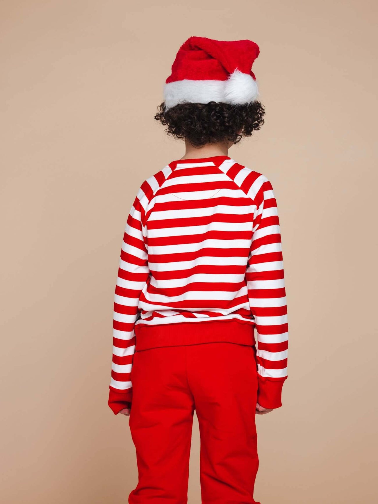 Kind in SNURK Pierre Xmas Sweater Kids met een kerstmannenmuts en gestreepte trui.