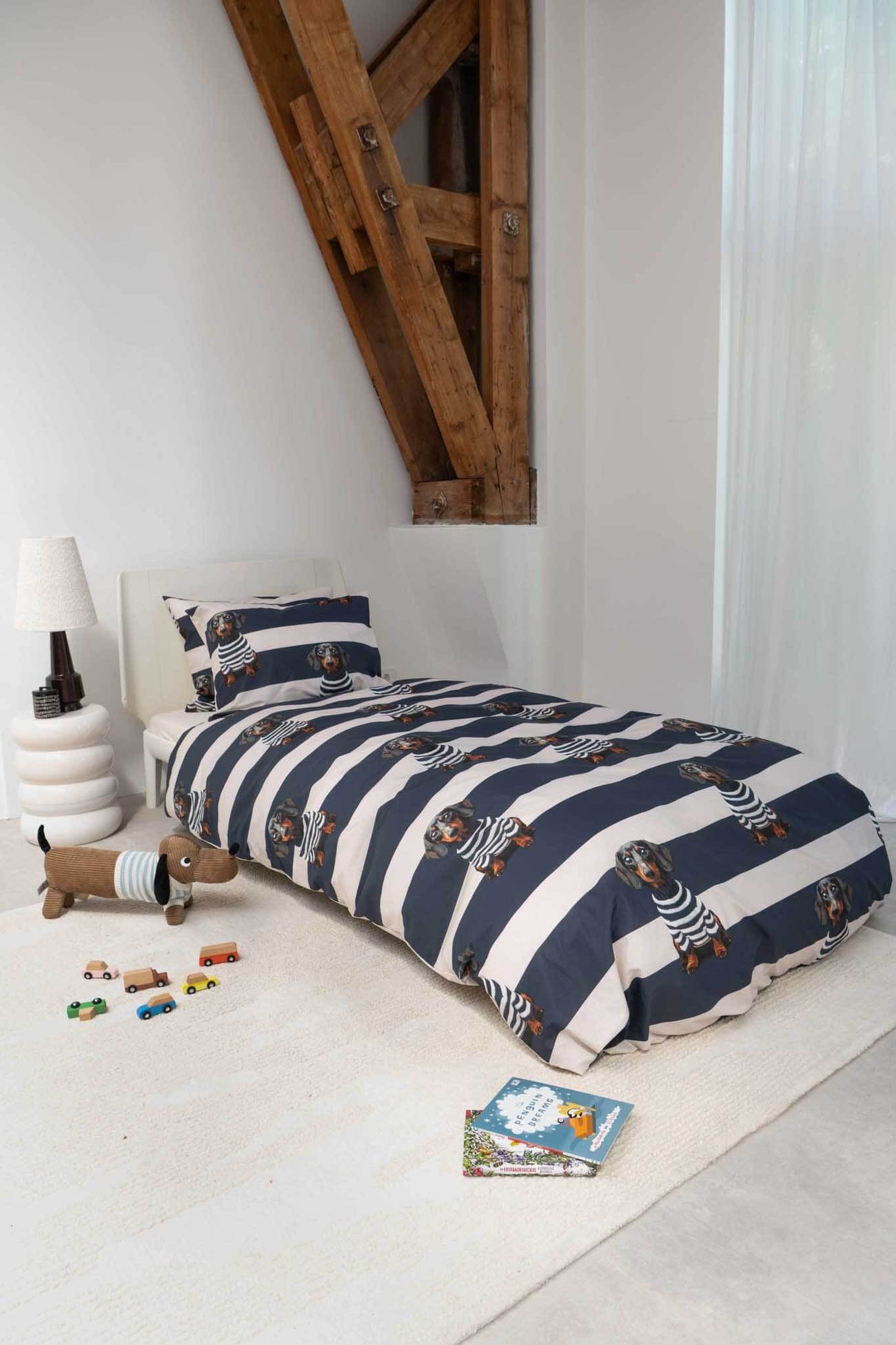 SNURK Pierre dekbedovertrek met gestreept ontwerp en teckelprint op bed in moderne slaapkamer.