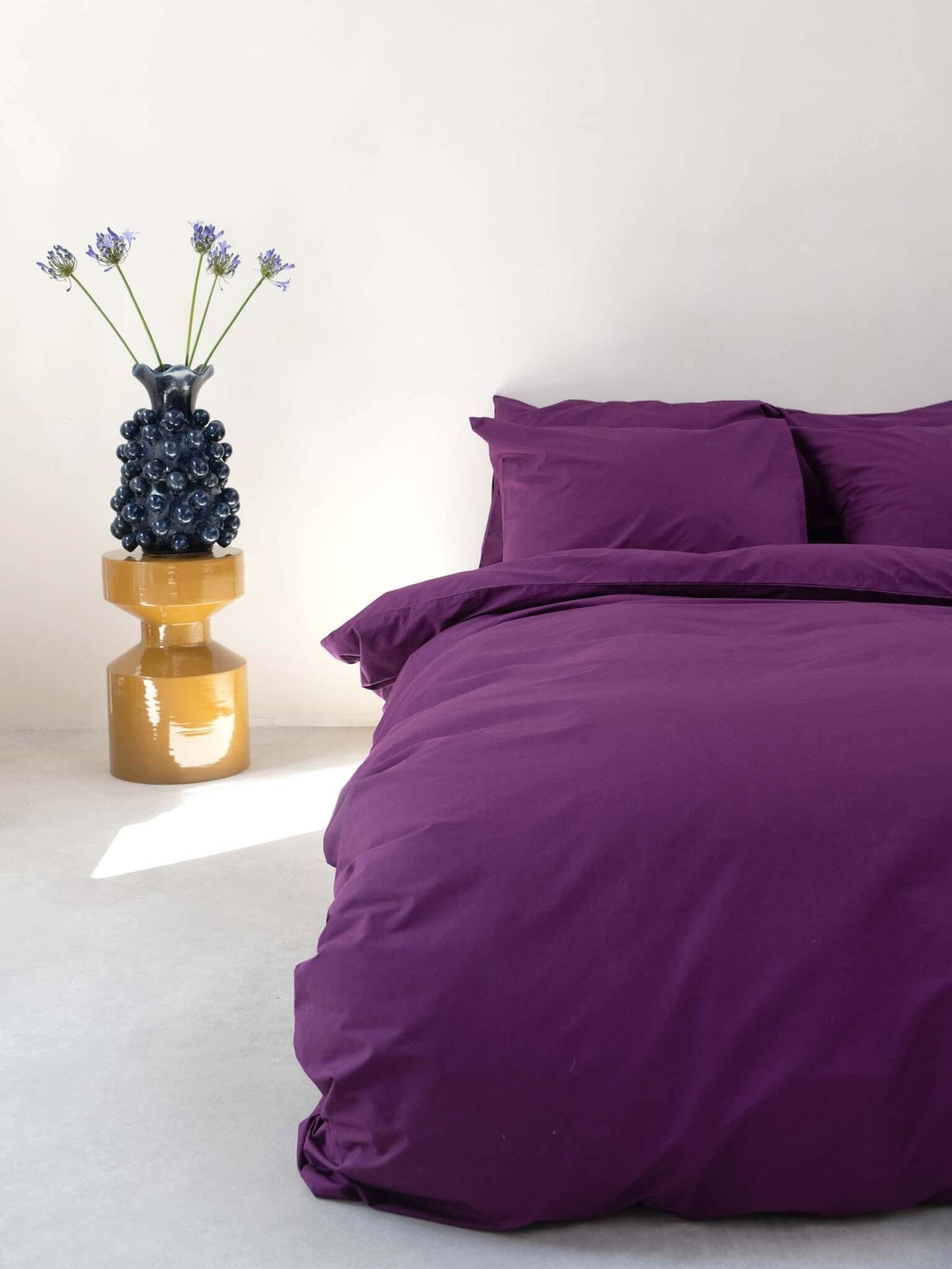 SNURK Plum Purple dekbedovertrek op een bed met een decoratieve vaas ernaast.