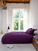 SNURK Plum Purple dekbedovertrek op bed in lichte slaapkamer met grote ramen.