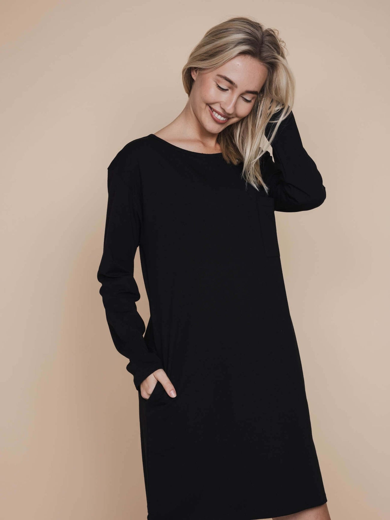 Model in SNURK Slow Black Long Sleeve Dress Dames, zwart nachthemd met lange mouwen en praktische zakken.