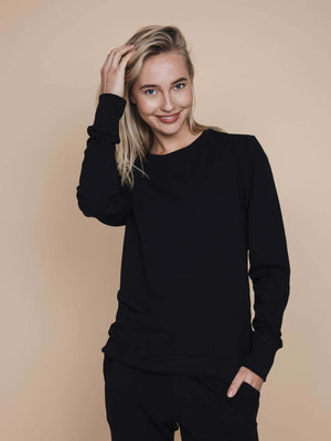 SNURK Slow Black Sweater Dames model in zwarte sweater met glimlach en hand door het haar.