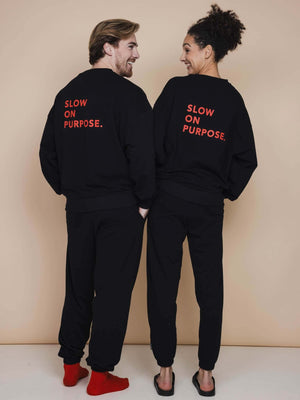 SNURK Slow Black Sweater Unisex model show, featuring 'SLOW ON PURPOSE' on the back in bright red.