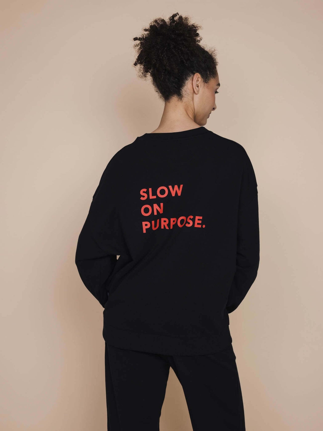 SNURK Slow Black Sweater Unisex met de tekst 'SLOW ON PURPOSE' op de rug in heldere letters.
