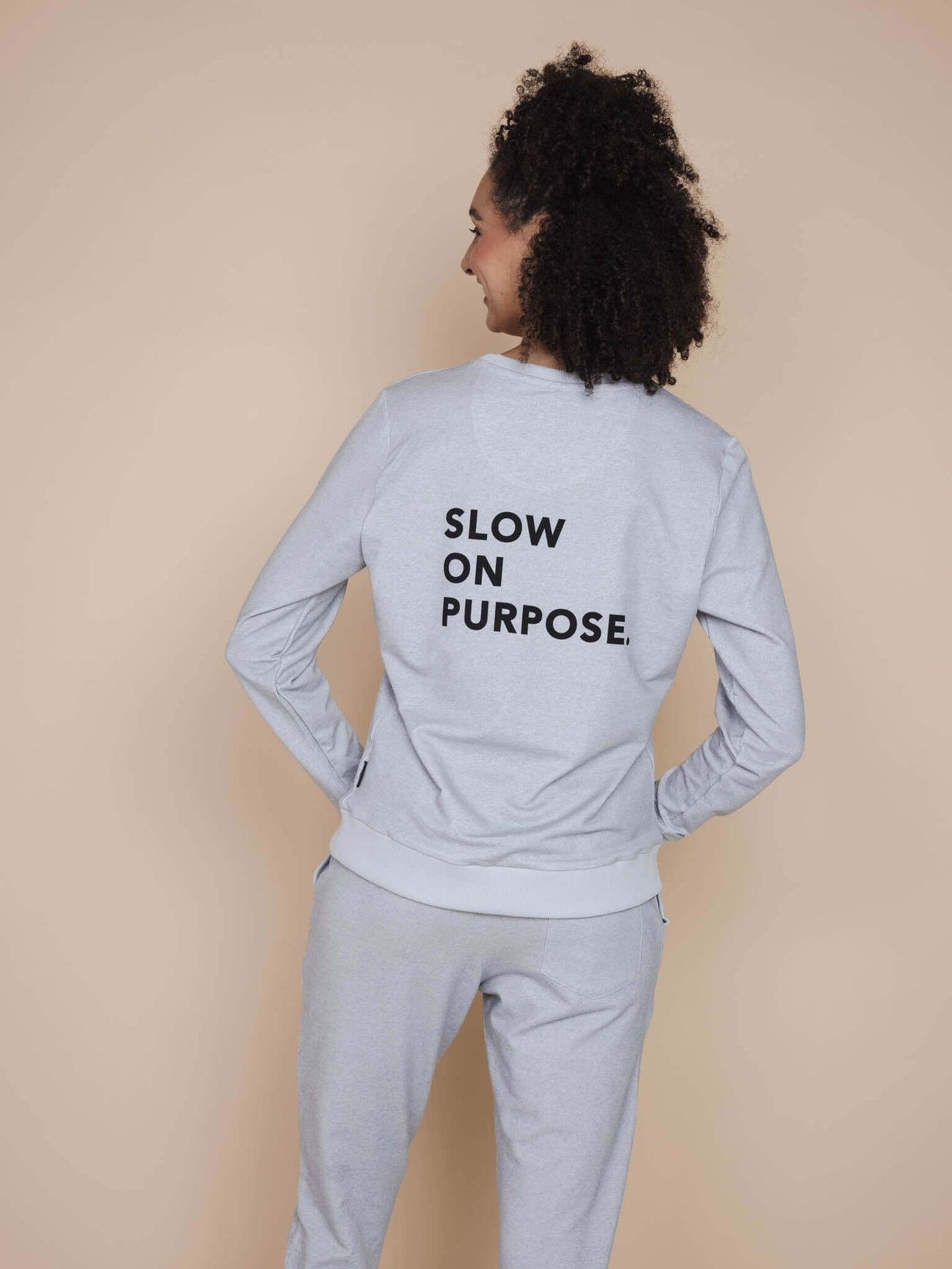 SNURK Slow Grey Sweater Dames met teksten 'SLOW ON PURPOSE' op de rug, vrouw in comfortabele outfit.