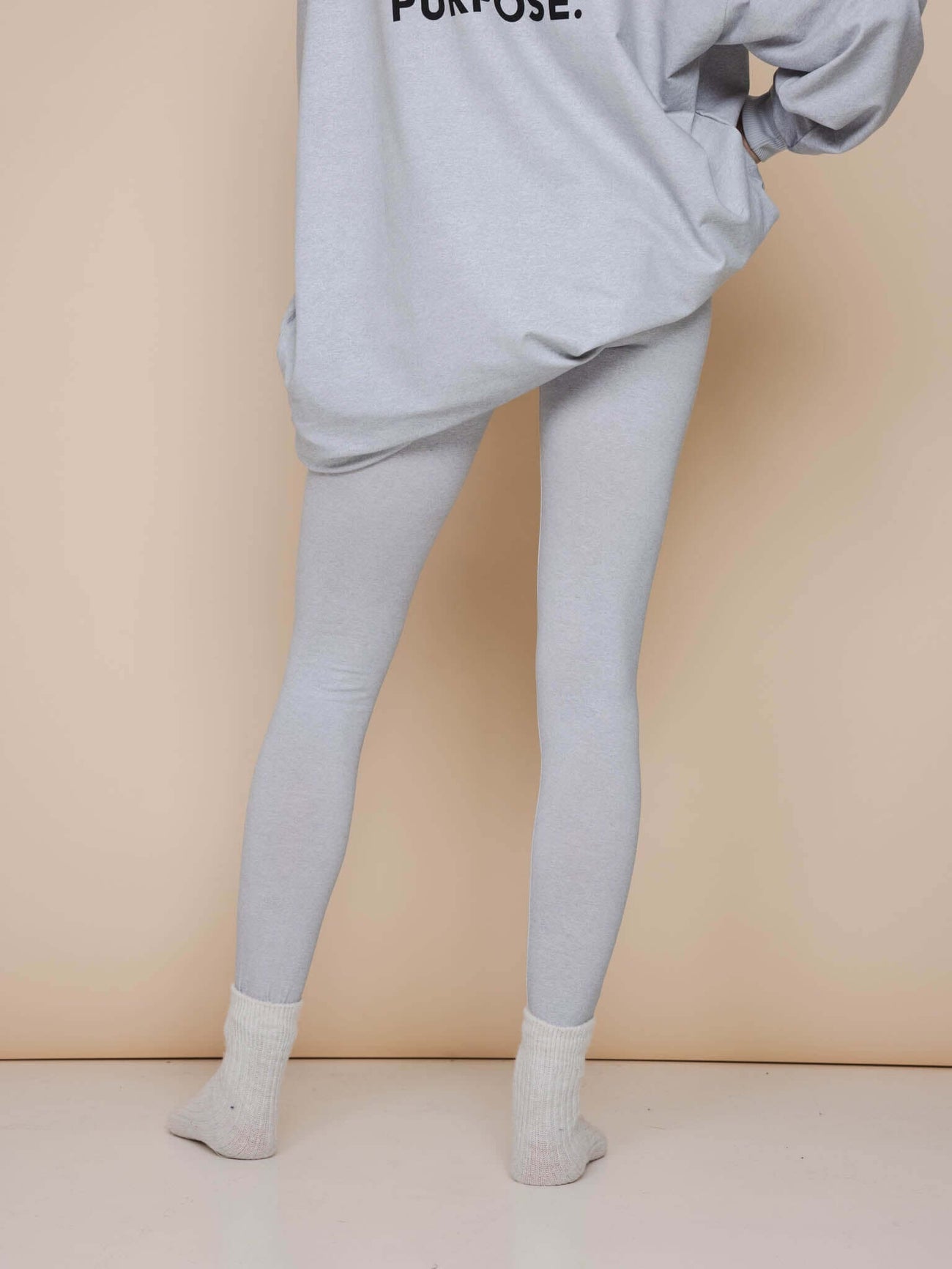 Model wearing SNURK Slow Grey Sweater Dress Dames with light gray leggings and cozy socks.