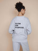 SNURK Slow Grey Sweater Unisex met tekst 'SLOW ON PURPOSE' op de rug.