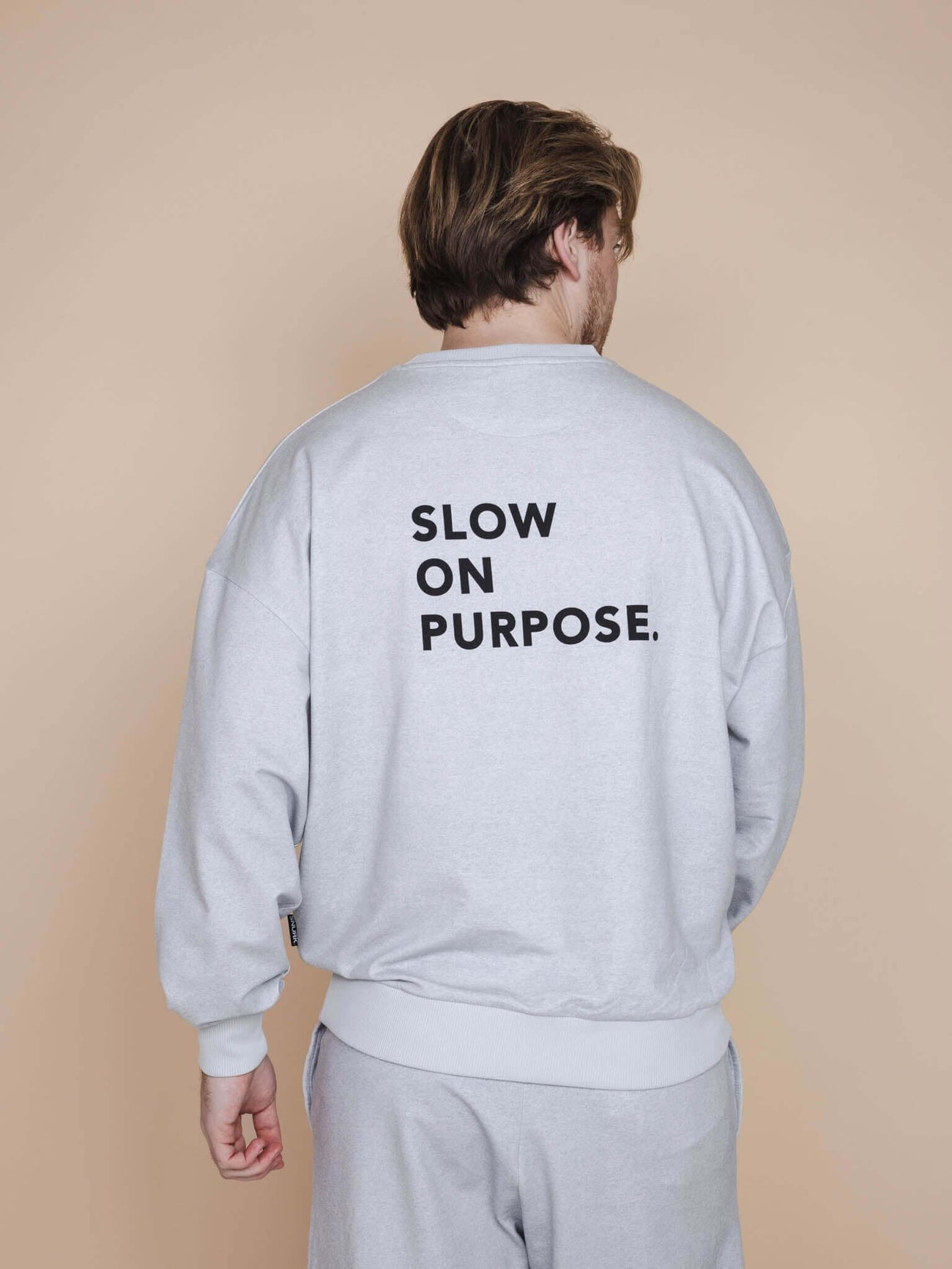 SNURK Slow Grey Sweater Unisex met 'SLOW ON PURPOSE.' op de rug, perfect voor een relaxdag.