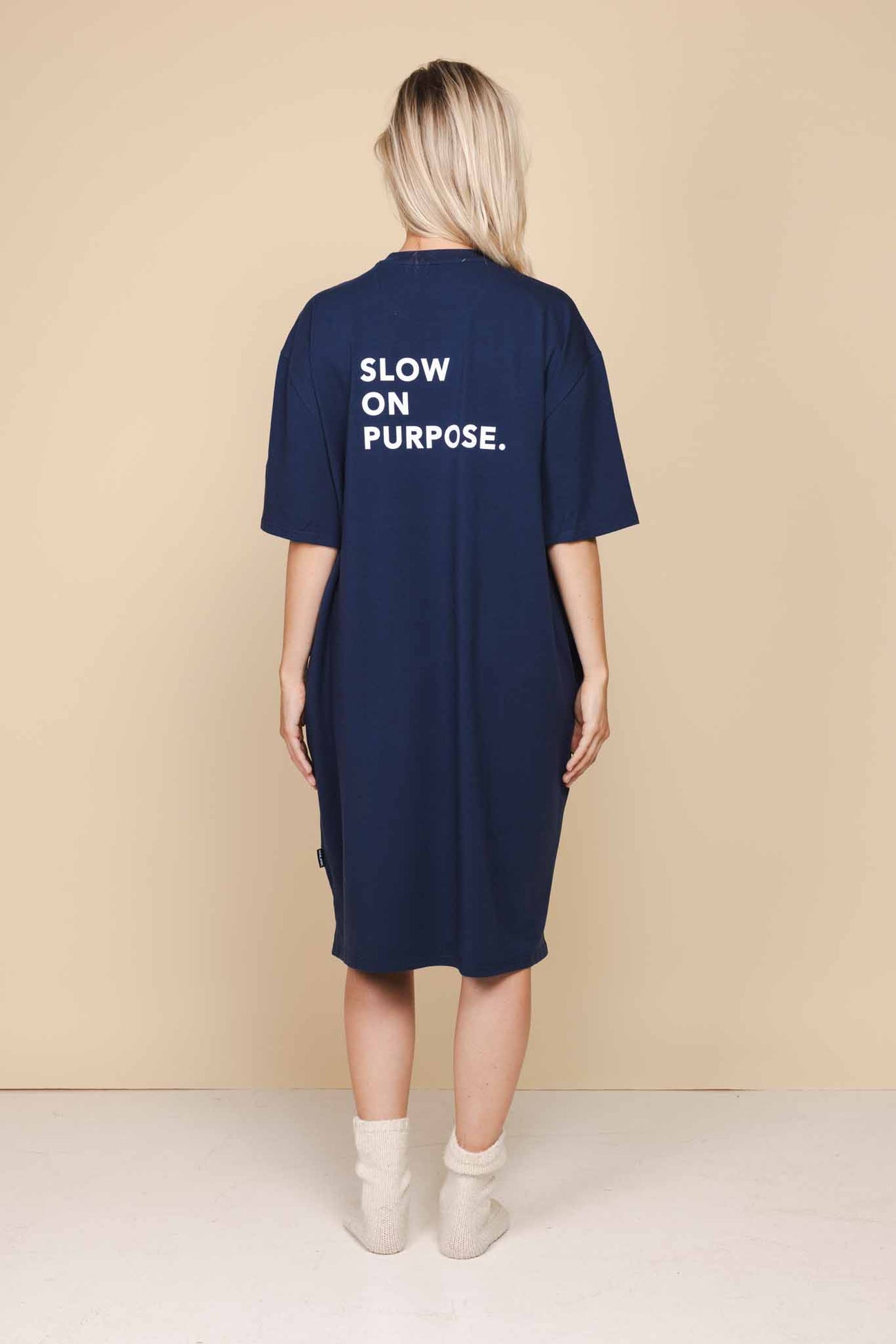 SNURK Slow Navy Relaxed Tee Dress Dames achterzijde met slogan Slow on Purpose op donkerblauwe jurk.