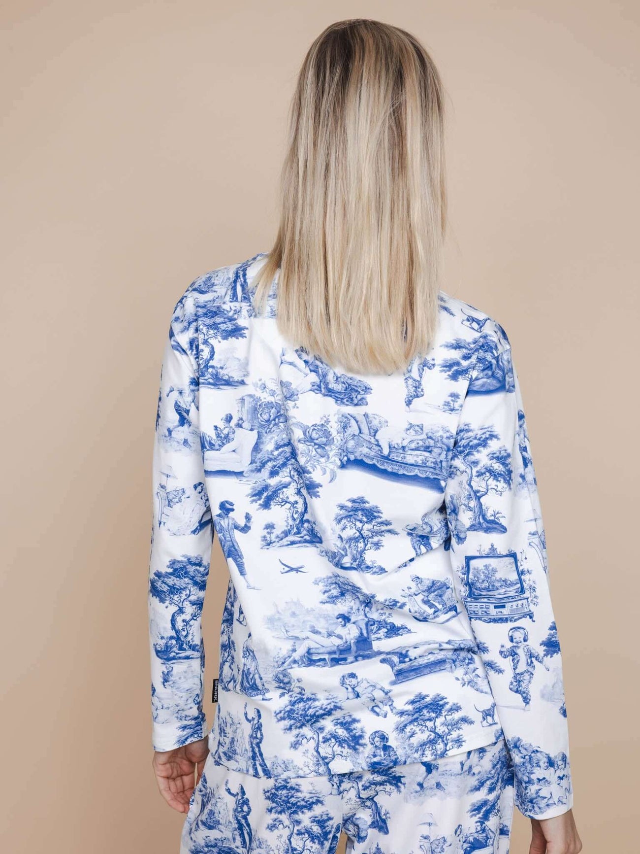 A woman wearing the SNURK Toile De Modern Joy Long Sleeve T-shirt Dames, featuring a unique blue and white design.
